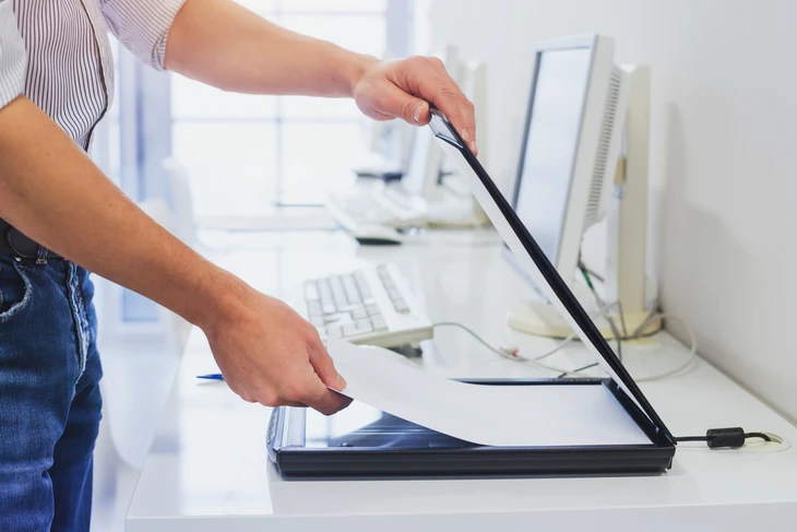 Personne en chemise rayée utilisant un scanner à plat professionnel dans un bureau moderne