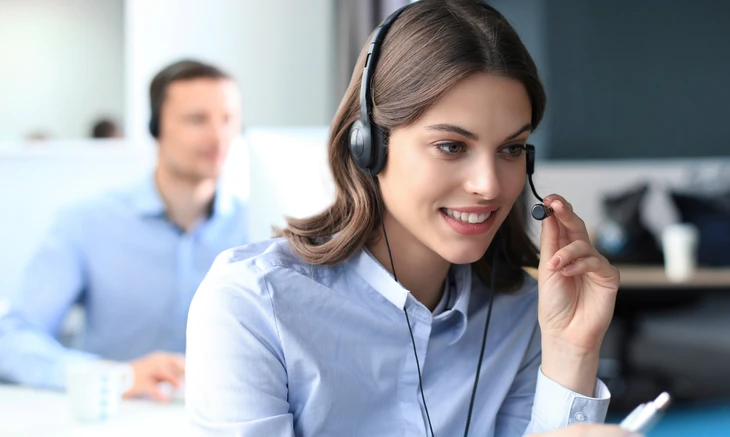 Employée de centre d'appel souriante avec casque micro, chemise bleue professionnelle, assistance téléphonique