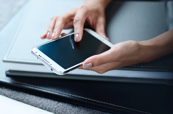Femme d'affaires manipulant une tablette tactile blanche sur un bureau, avec ordinateur portable et documents en arrière-plan
