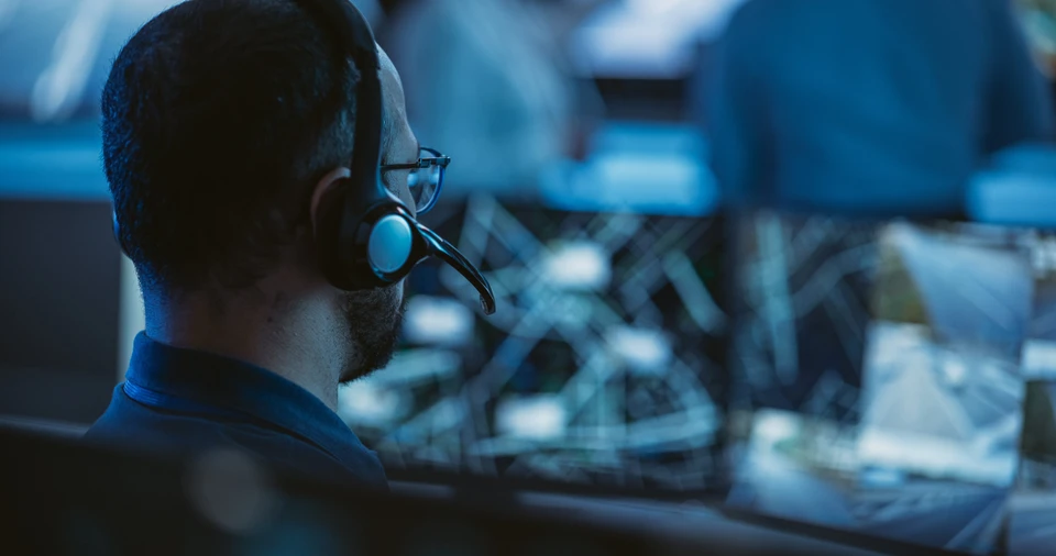 Le spécialiste technique du support à la clientèle parle sur un casque pendant qu'il travaille sur un ordinateur dans une salle de contrôle du centre d'appels, des écrans d'affichage remplis et des serveurs de données