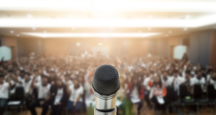 Salle de conférence avec public nombreux assis, éclairage de scène professionnel, atmosphère de présentation d'entreprise ou événement corporatif