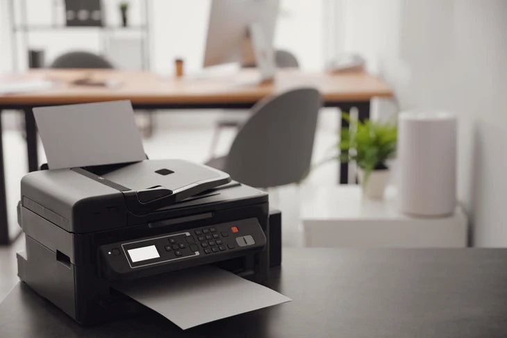 Bureau moderne avec imprimante multifonction professionnelle noire au premier plan, équipée d'écran LCD, clavier numérique et bac papier