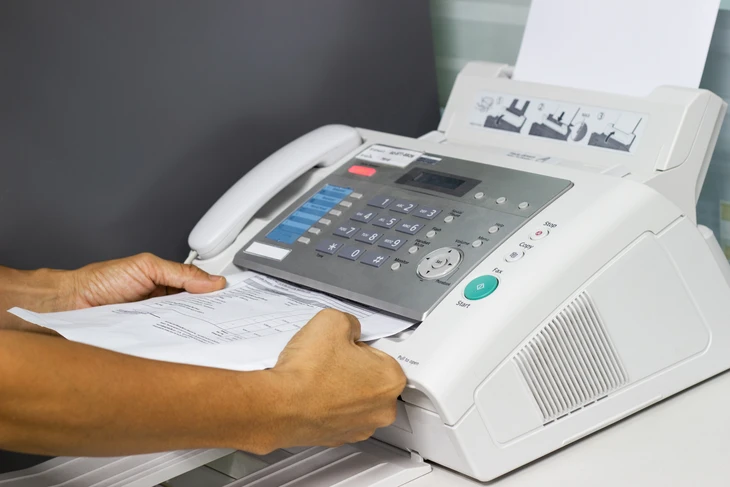 Personne utilisant un télécopieur multifonction dans un bureau, insérant des documents papier dans l'appareil