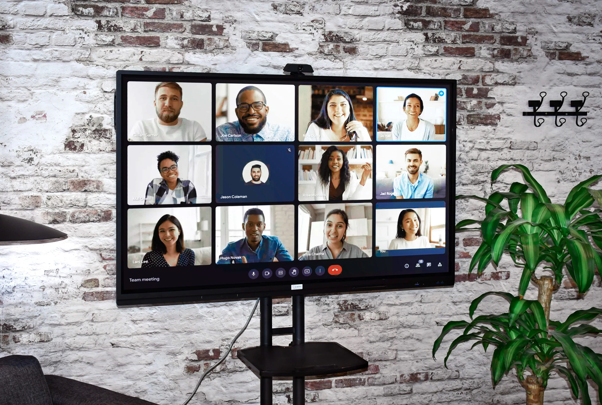 Photographie d'un professionnel en costume présentant ou pointant du doigt un grand écran interactif haute résolution montant du contenu collaboratif (graphiques, interface de conférence ou présentation visuelle), dans une salle de réunion moderne avec une table de conférence en arrière-plan, éclairage professionnel naturel, ambiance sérieuse et contemporaine.