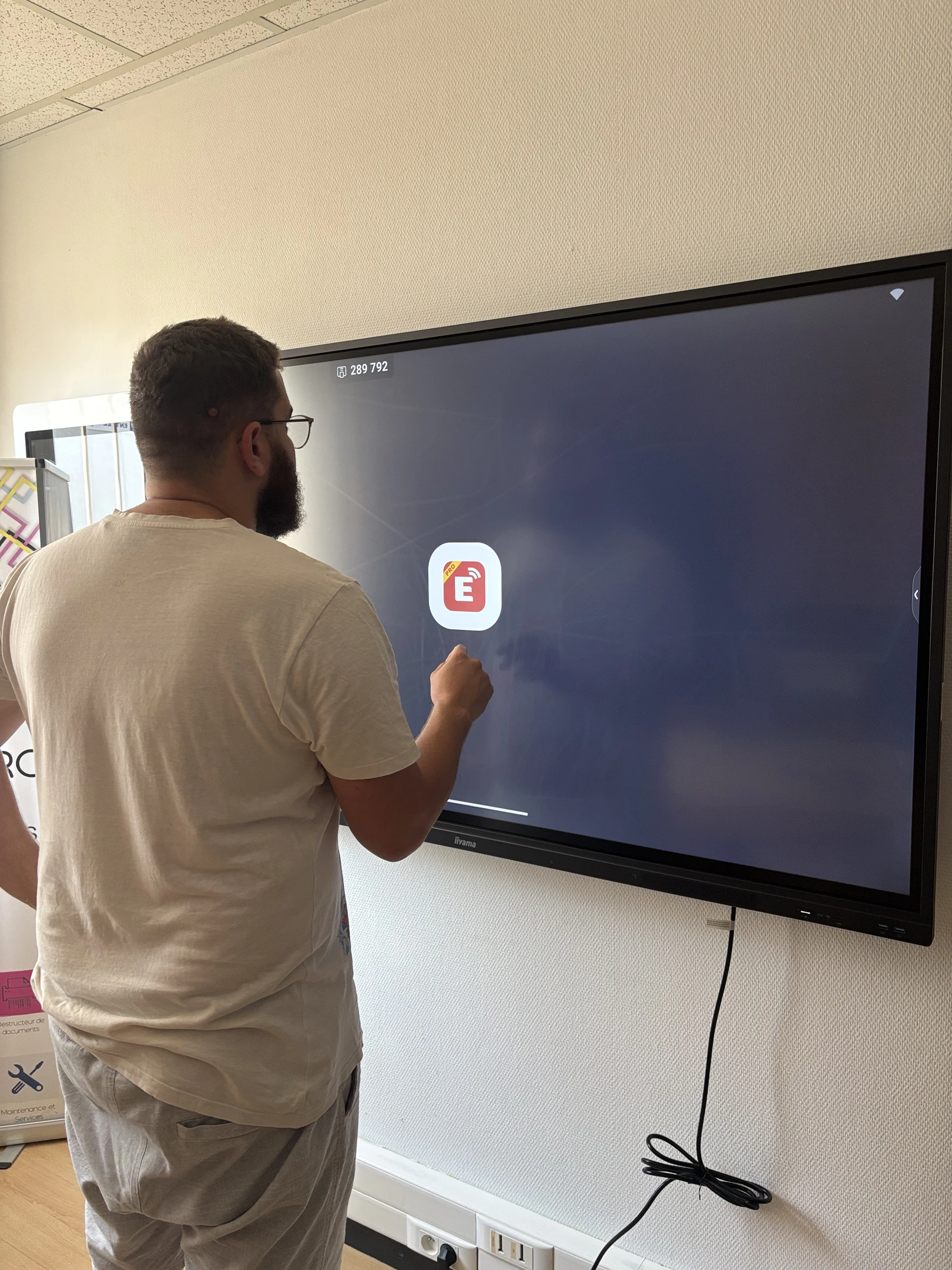 Réunion d'équipe en bureau moderne avec femme debout présentant sur tablette numérique à quatre collègues assis autour d'une table de travail